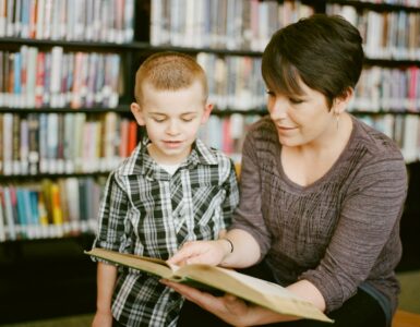 A student and adult read together in a library while discussing a passage for reciprocal teaching.