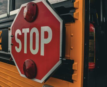 Close-up of a red stop sign extended from the side of a yellow school bus.