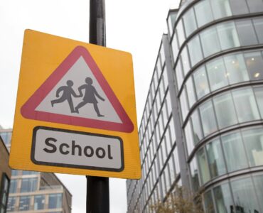 A school crossing sign with a reduced speed limit near a road and building.