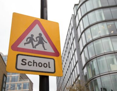 A school crossing sign with a reduced speed limit near a road and building.