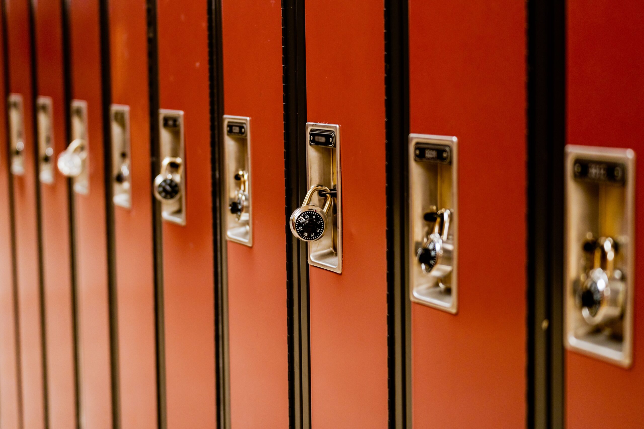 A row of school lockers secured with combination padlocks in a hallway.