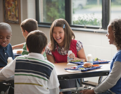 Middle school students eating school lunches with milk in a cafeteria.