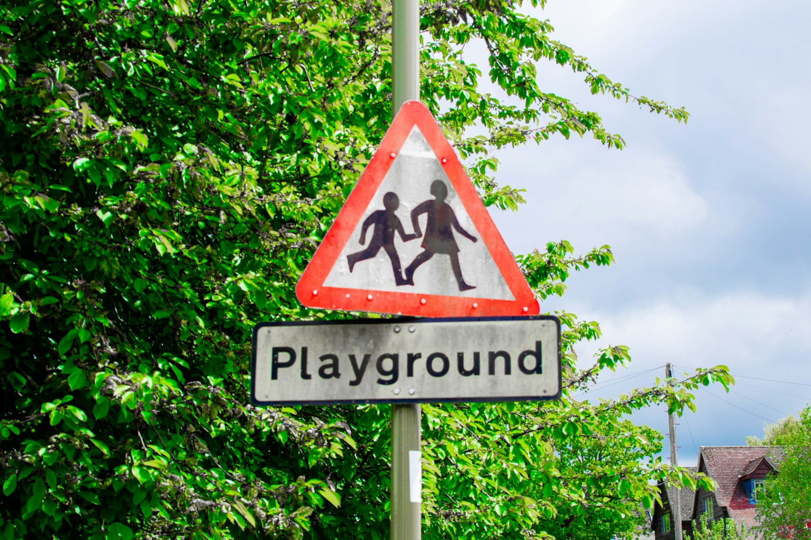 A yellow pedestrian warning sign near trees in a school or neighborhood area.