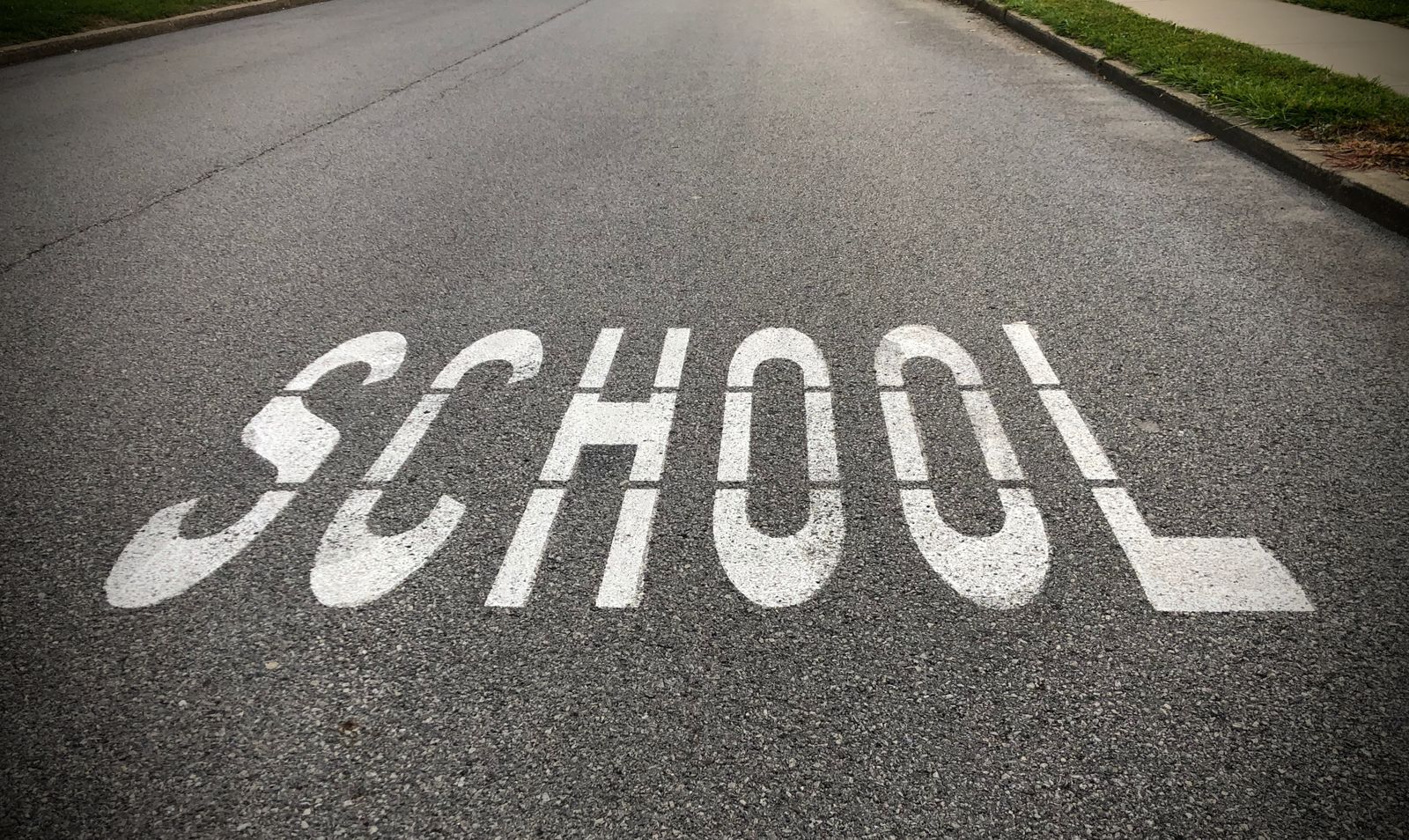 A school zone road marking on pavement near a crossing area.