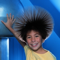 A student touches a Van de Graaff generator while charged hair strands repel one another and stand outward.