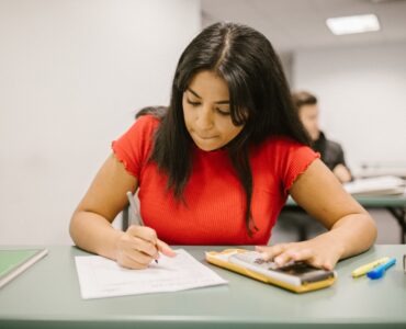 A student uses a calculator and notes to work out a weighted course average.