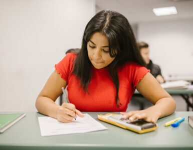 A student uses a calculator and notes to work out a weighted course average.