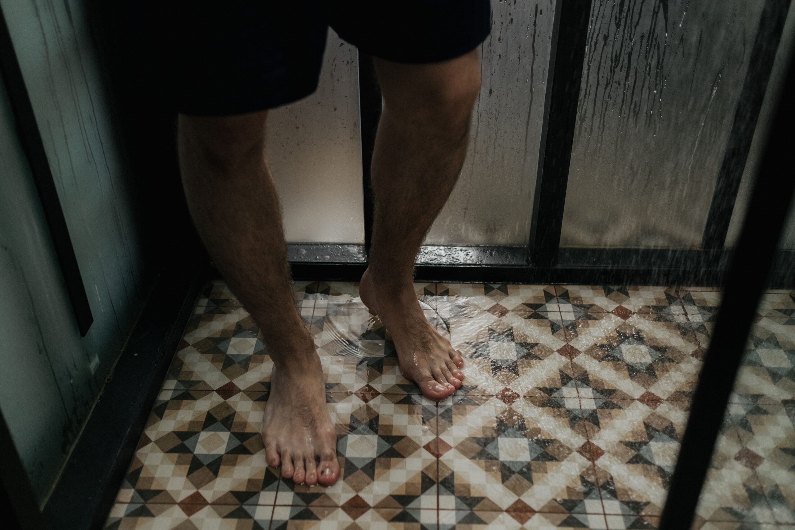Bare feet on a wet tiled shower floor, showing the kind of damp surface where shower shoes provide a barrier.