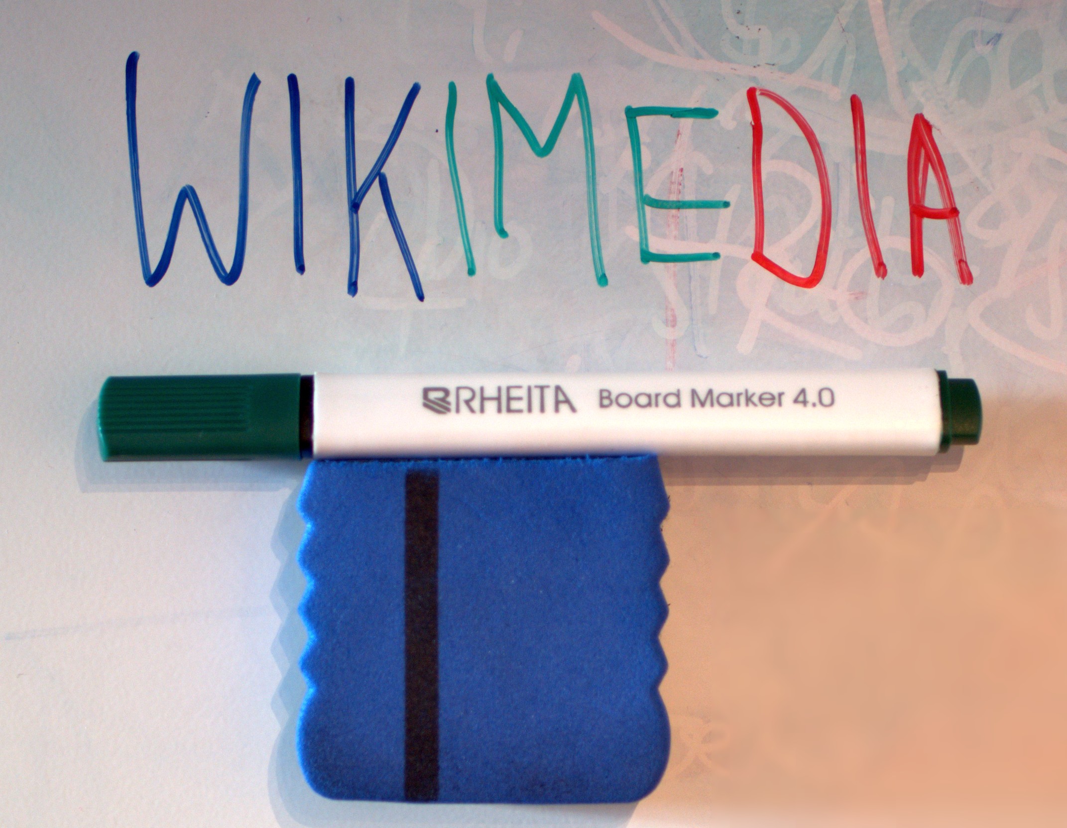 A dry-erase marker and eraser beside colored writing on a whiteboard.