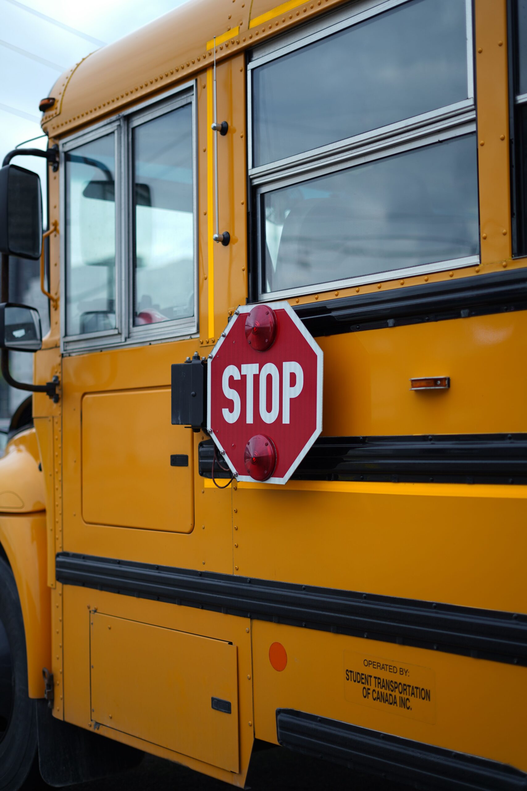 Side view of a yellow school bus with a red stop sign mounted near the windows.