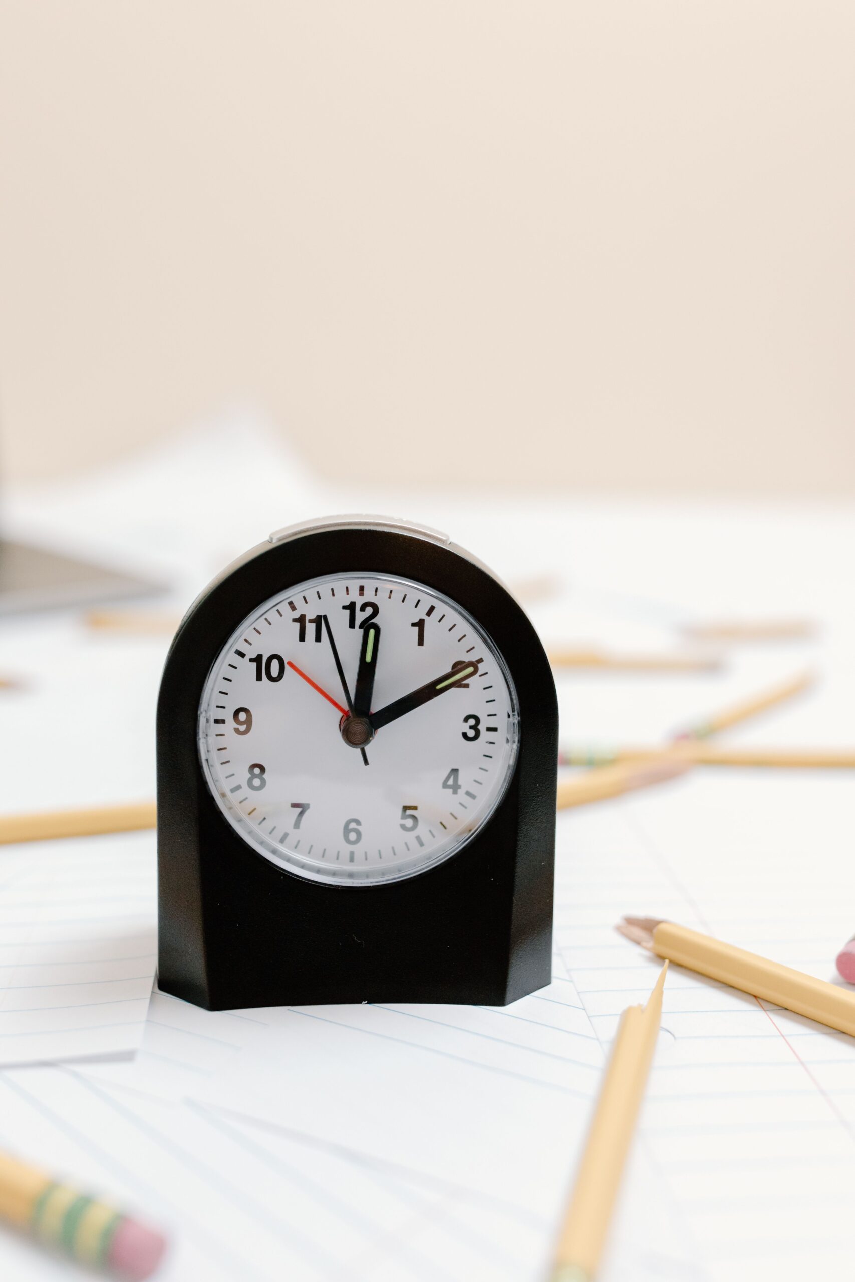 A black analog clock rests on papers beside pencils at a study desk.