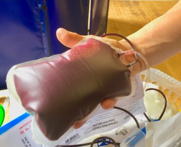 A nurse holding a freshly donated unit of blood beside sample tubes used for safety testing.