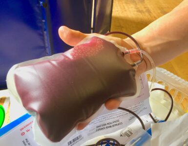 A nurse holding a freshly donated unit of blood beside sample tubes used for safety testing.