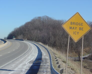 A yellow warning sign tells drivers that the bridge may be icy before the road.