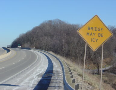 A yellow warning sign tells drivers that the bridge may be icy before the road.