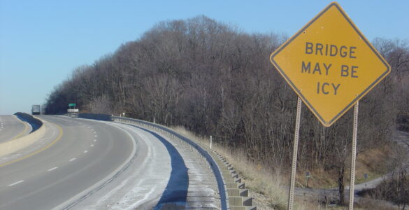 A yellow warning sign tells drivers that the bridge may be icy before the road.