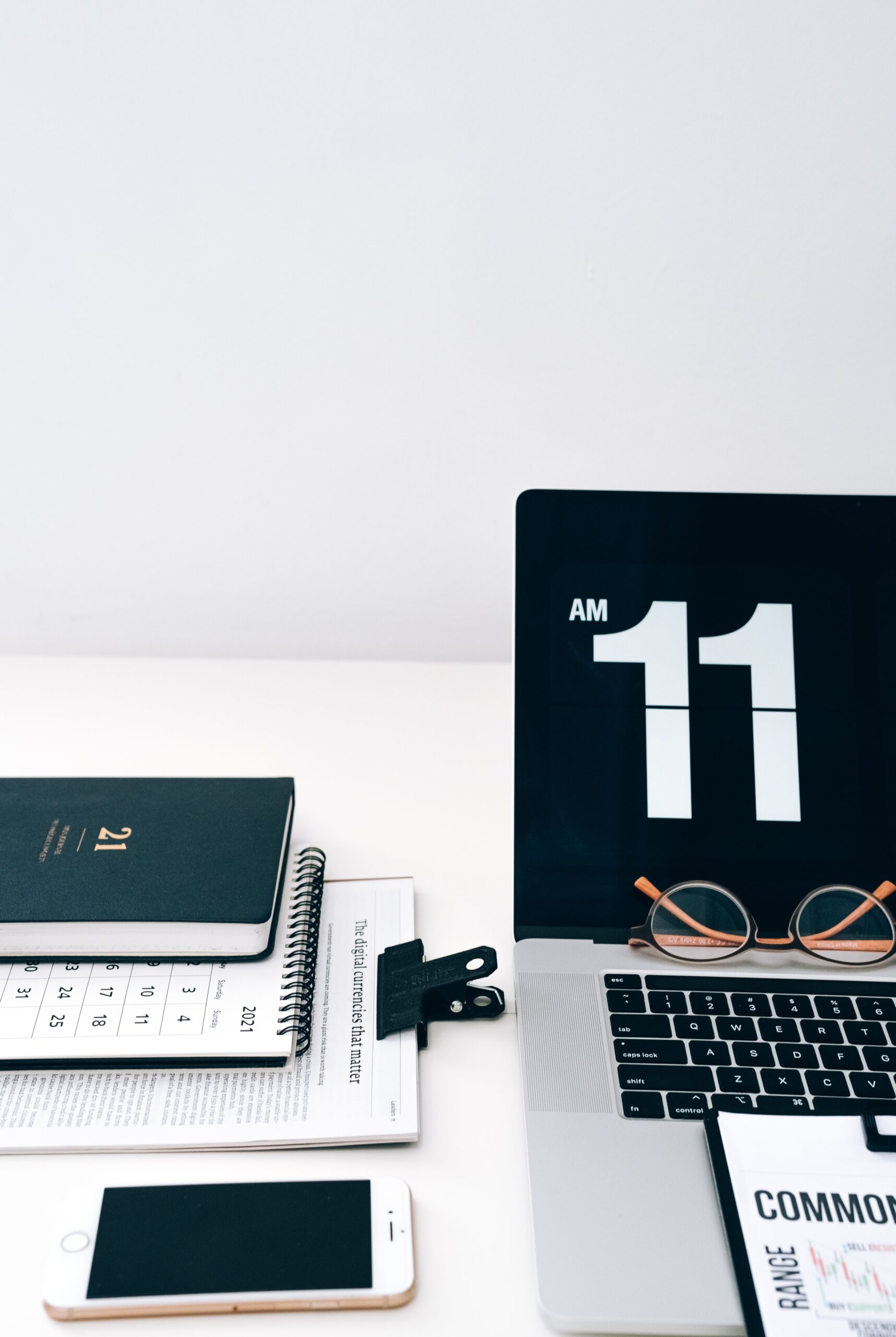 A laptop, phone, paper calendar, and digital clock arranged on a desk.