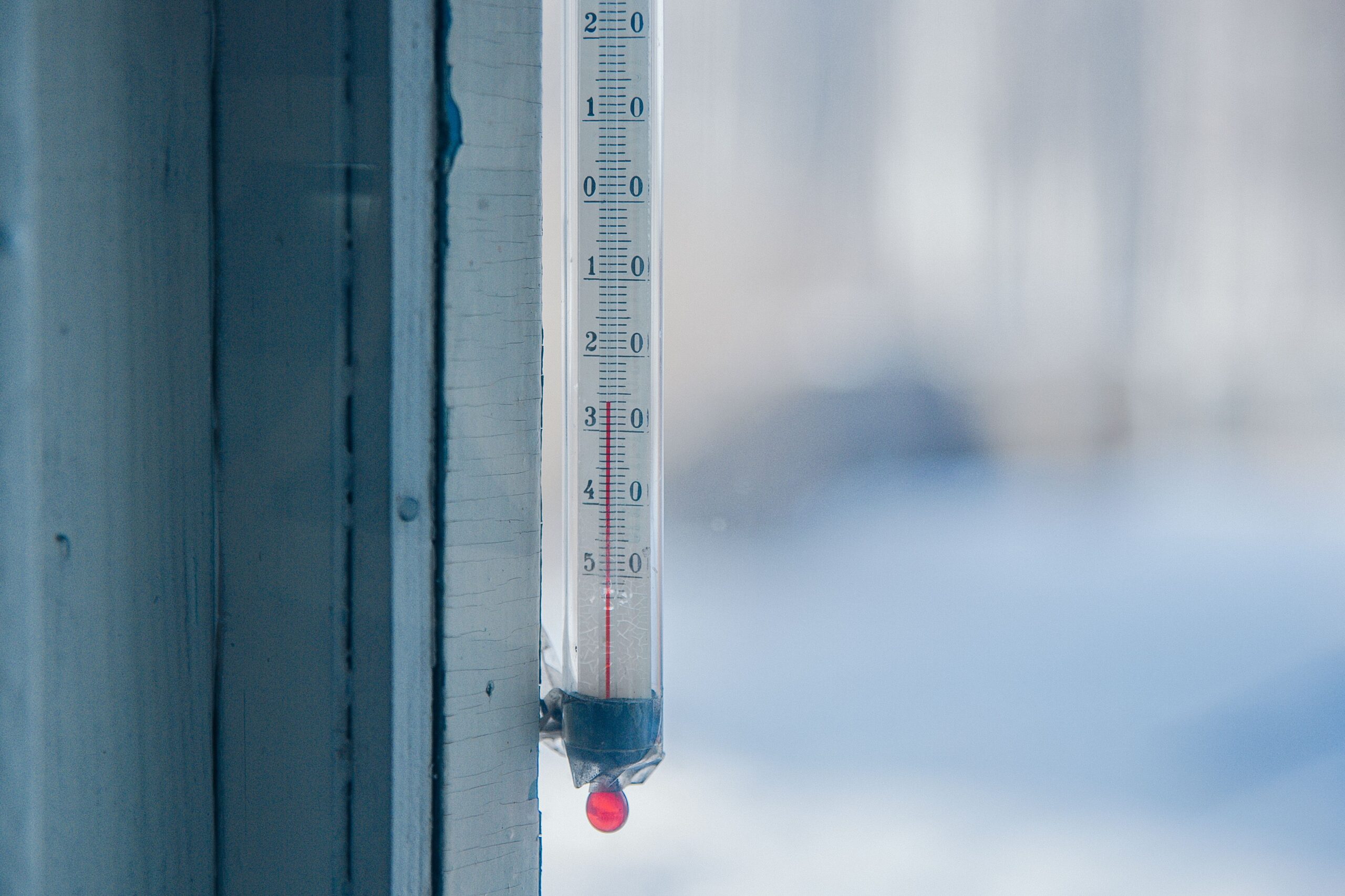 An outdoor thermometer stands against a frosty background near freezing temperatures.