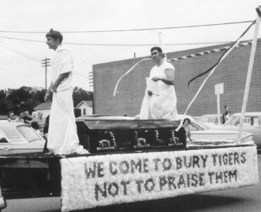 Two students in costume ride on an Arlington State College homecoming float, showing how pageantry became part of school tradition.