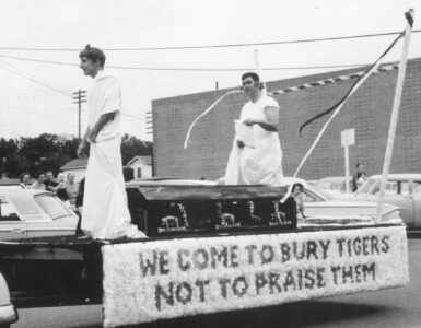 Two students in costume ride on an Arlington State College homecoming float, showing how pageantry became part of school tradition.
