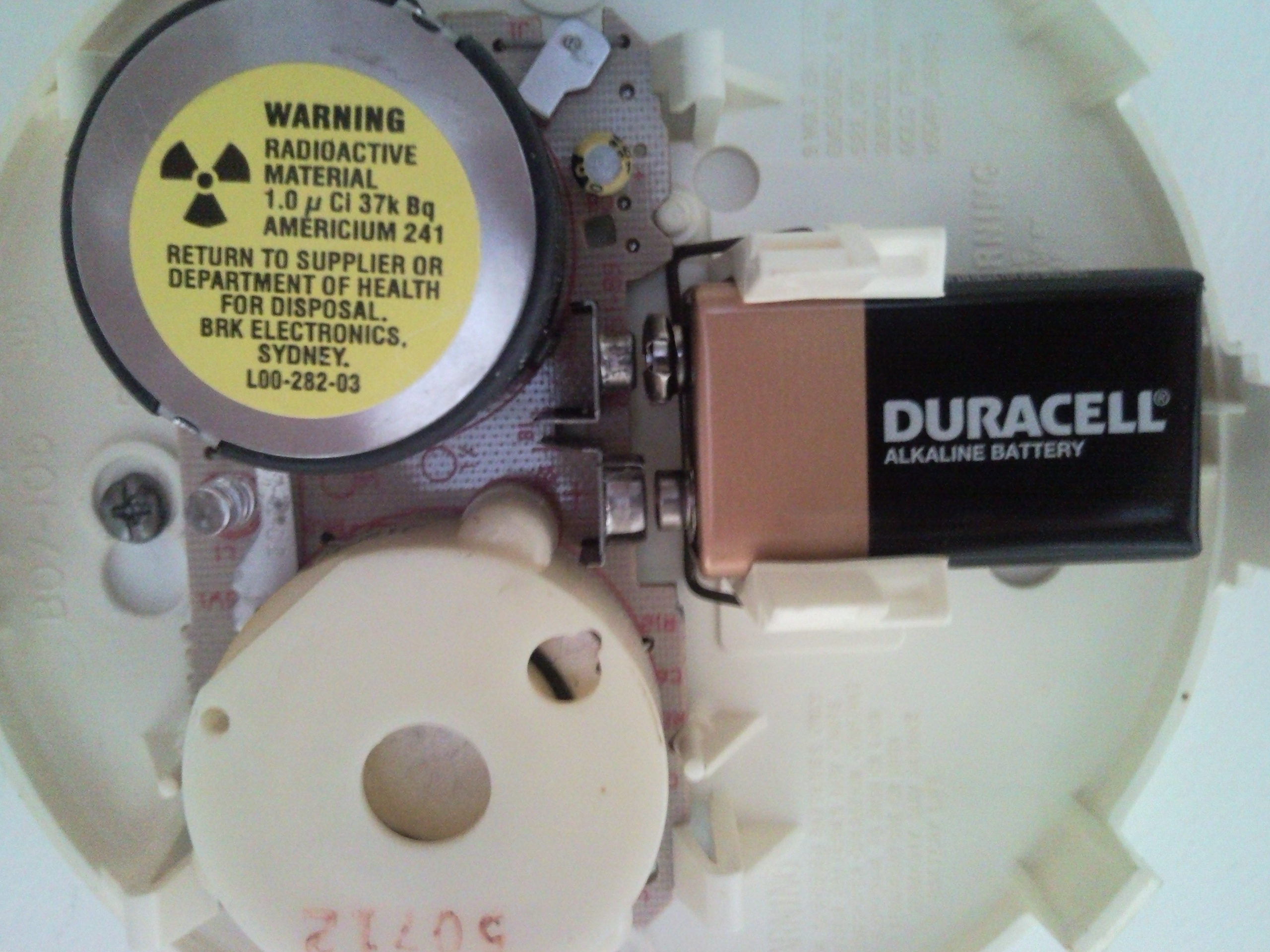 The inside of a smoke detector showing its circuit board and nine-volt battery.