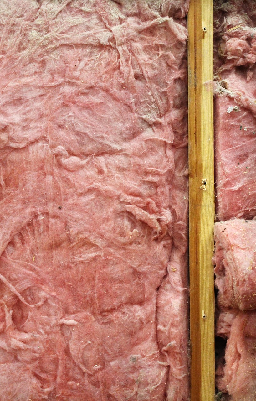 Pink insulation fitted between wooden studs in an unfinished wall.