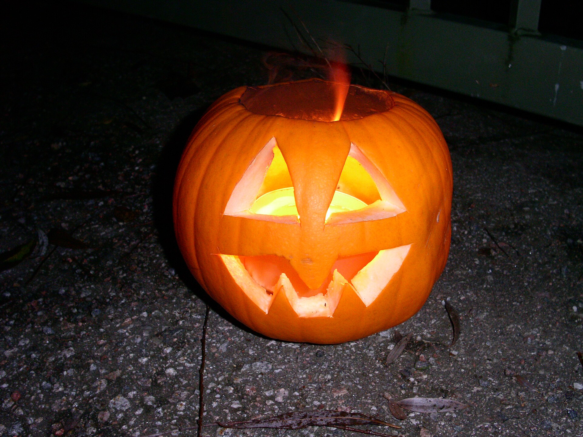 A candle-lit jack-o'-lantern resting on an outdoor stone surface.