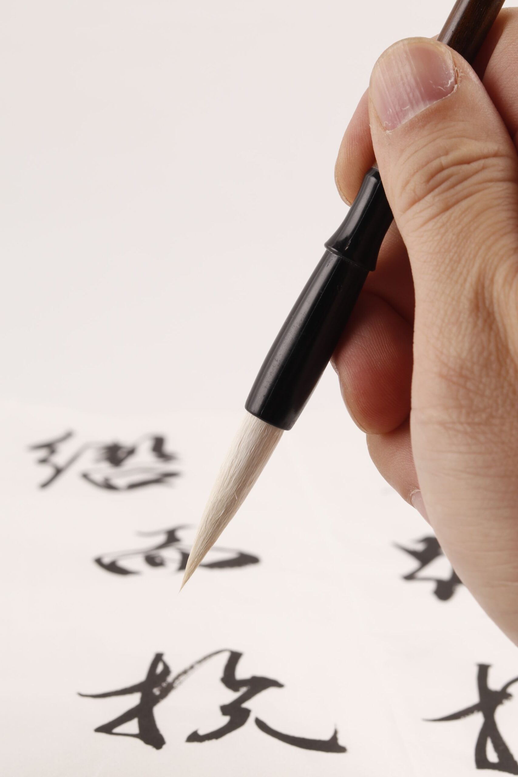 A hand writes Japanese words with kanji and kana on study paper.