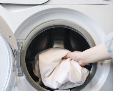 A hand placing clothing into a front-loading washing machine.