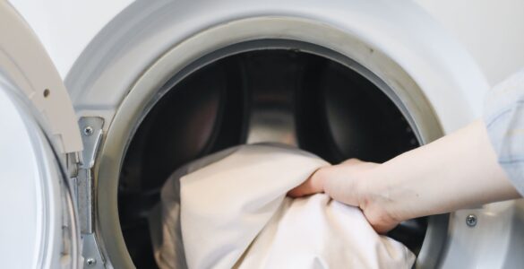 A hand placing clothing into a front-loading washing machine.