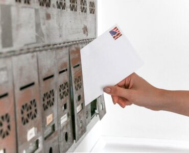 A voter placing a stamped mail ballot envelope into a mailbox