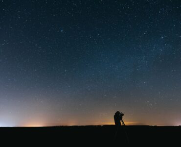 A person using a telescope under a star-filled night sky while looking for a faint planet.