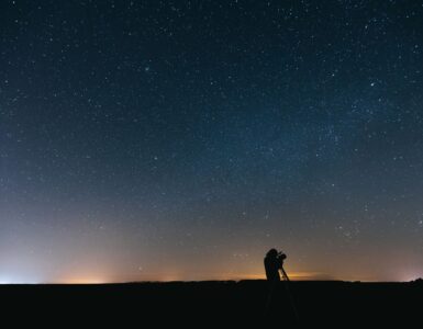 A person using a telescope under a star-filled night sky while looking for a faint planet.