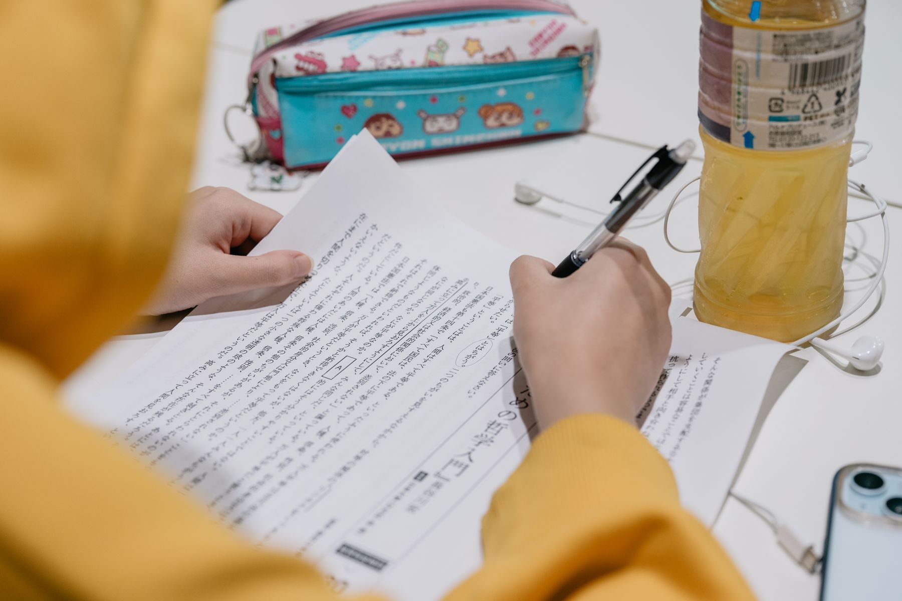 A learner studies Japanese text and records kanji readings in a notebook.