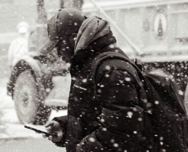 A person checks a smartphone while walking along a snowy city street