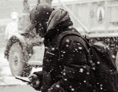 A person checks a smartphone while walking along a snowy city street