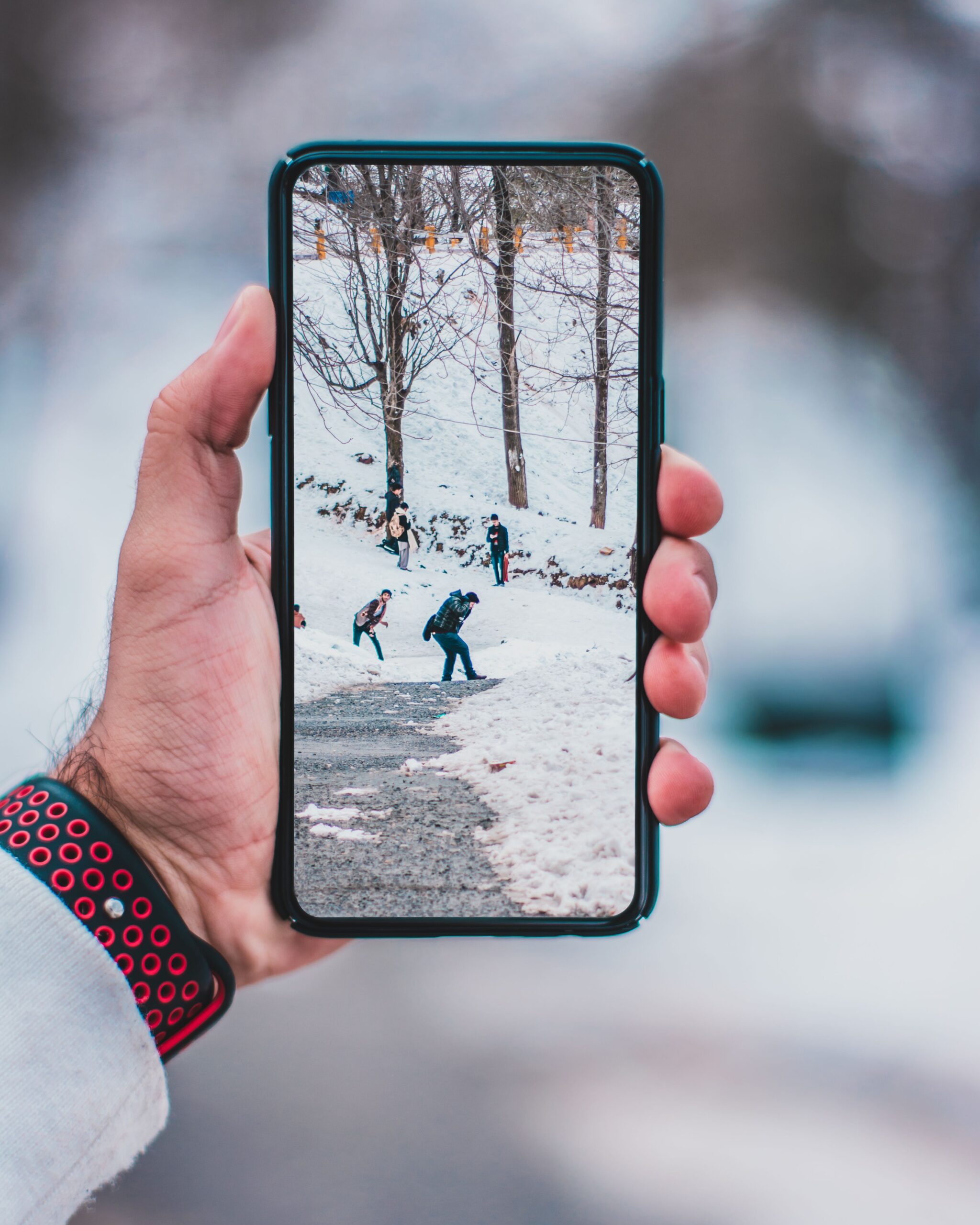 A person holds a smartphone displaying a snow-covered walking path
