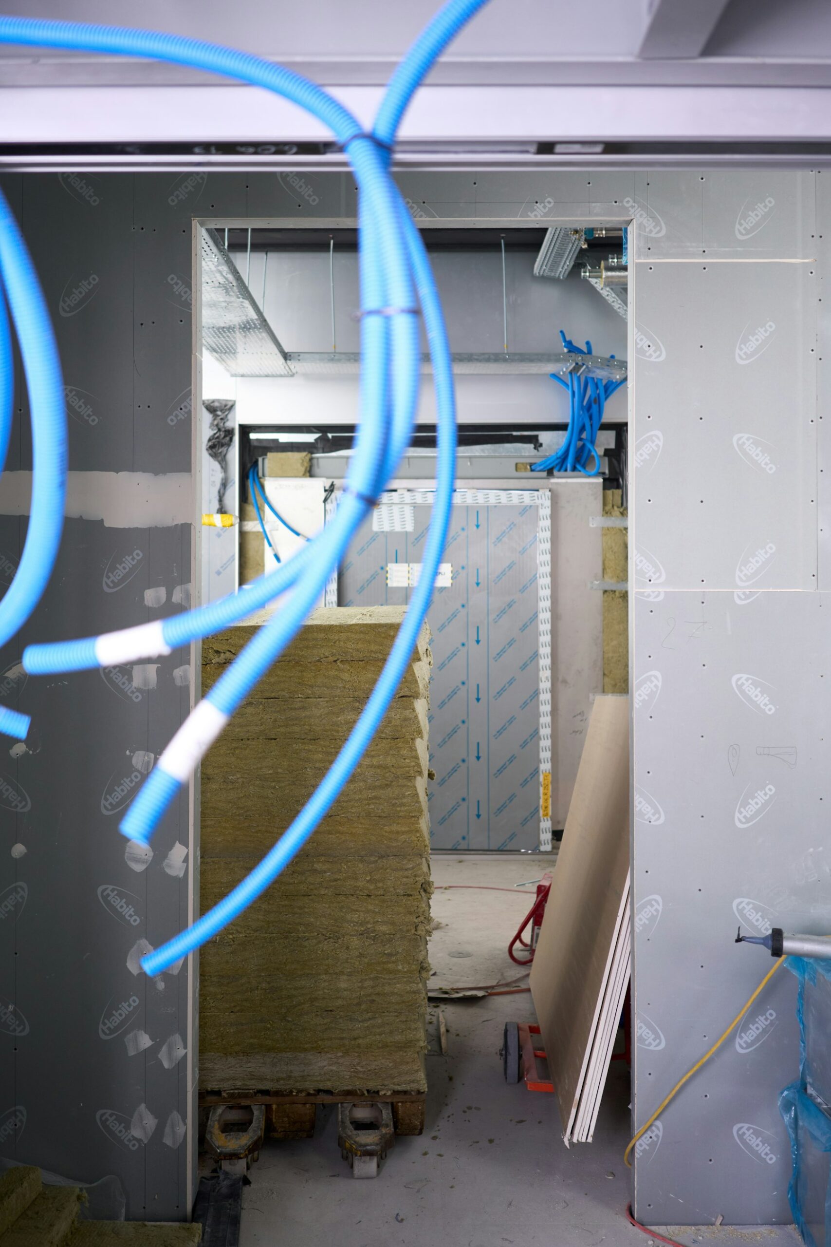 Blue building pipes pass through insulation and framing at a construction site.