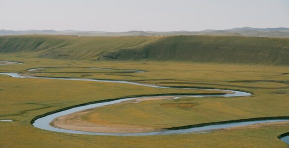 A winding river crosses a broad floodplain, showing bends shaped by erosion and sediment deposition.
