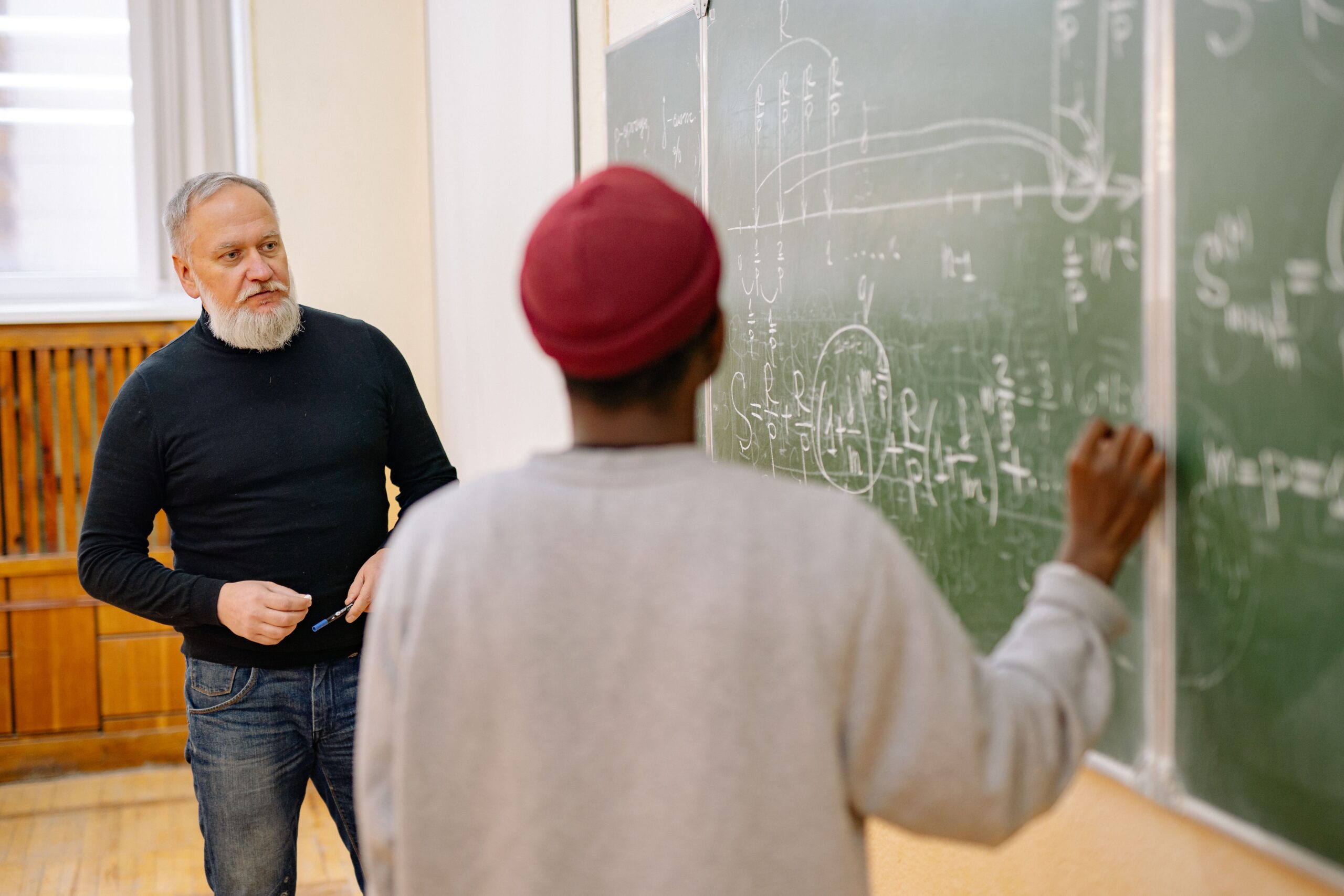 Teacher and student examining equations on a classroom blackboard