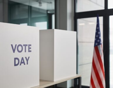 Voting booths and an American flag at a polling place, representing how registration records prepare voters for Election Day.