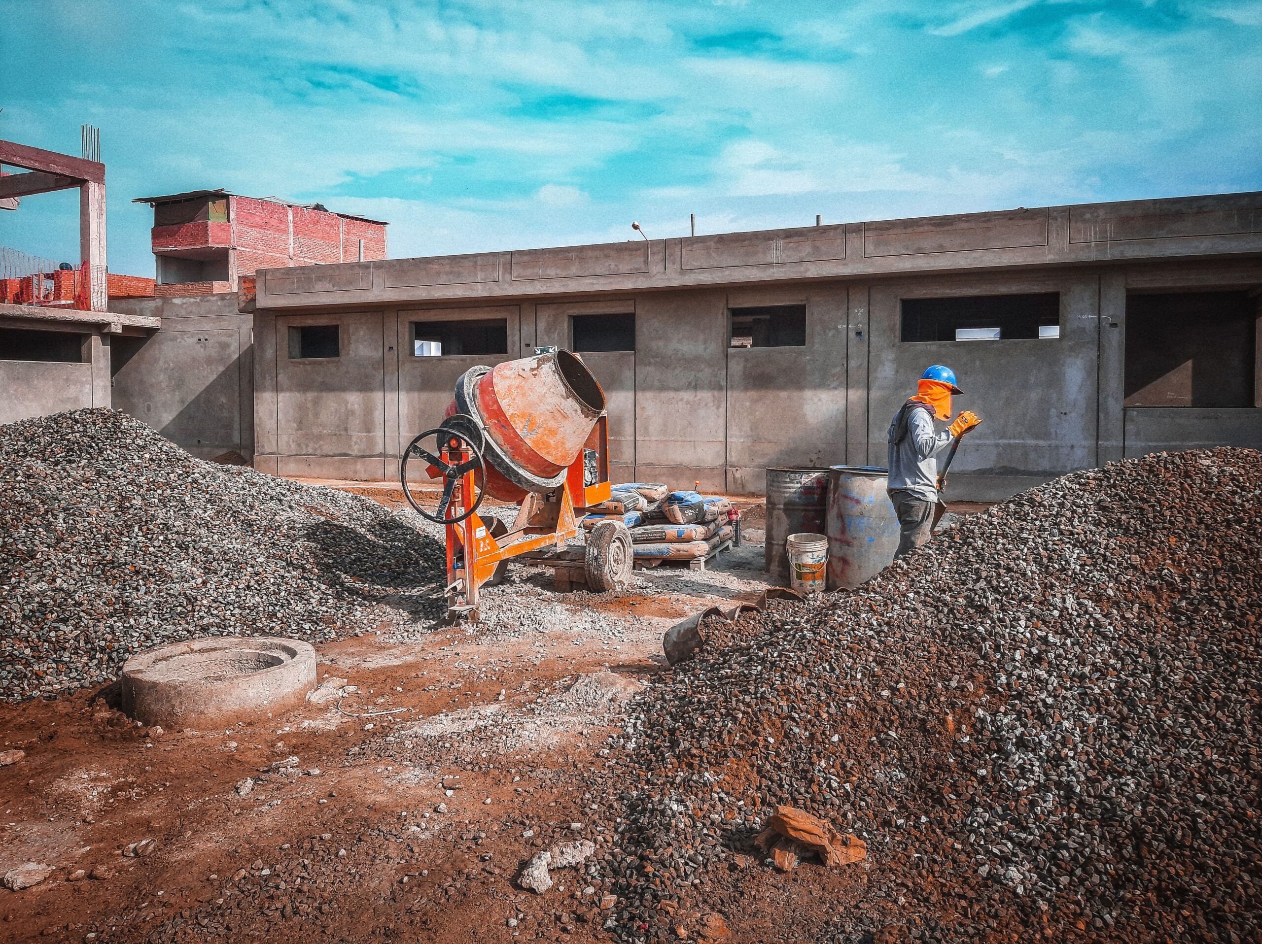 Worker beside a cement mixer and piles of aggregate at a construction site