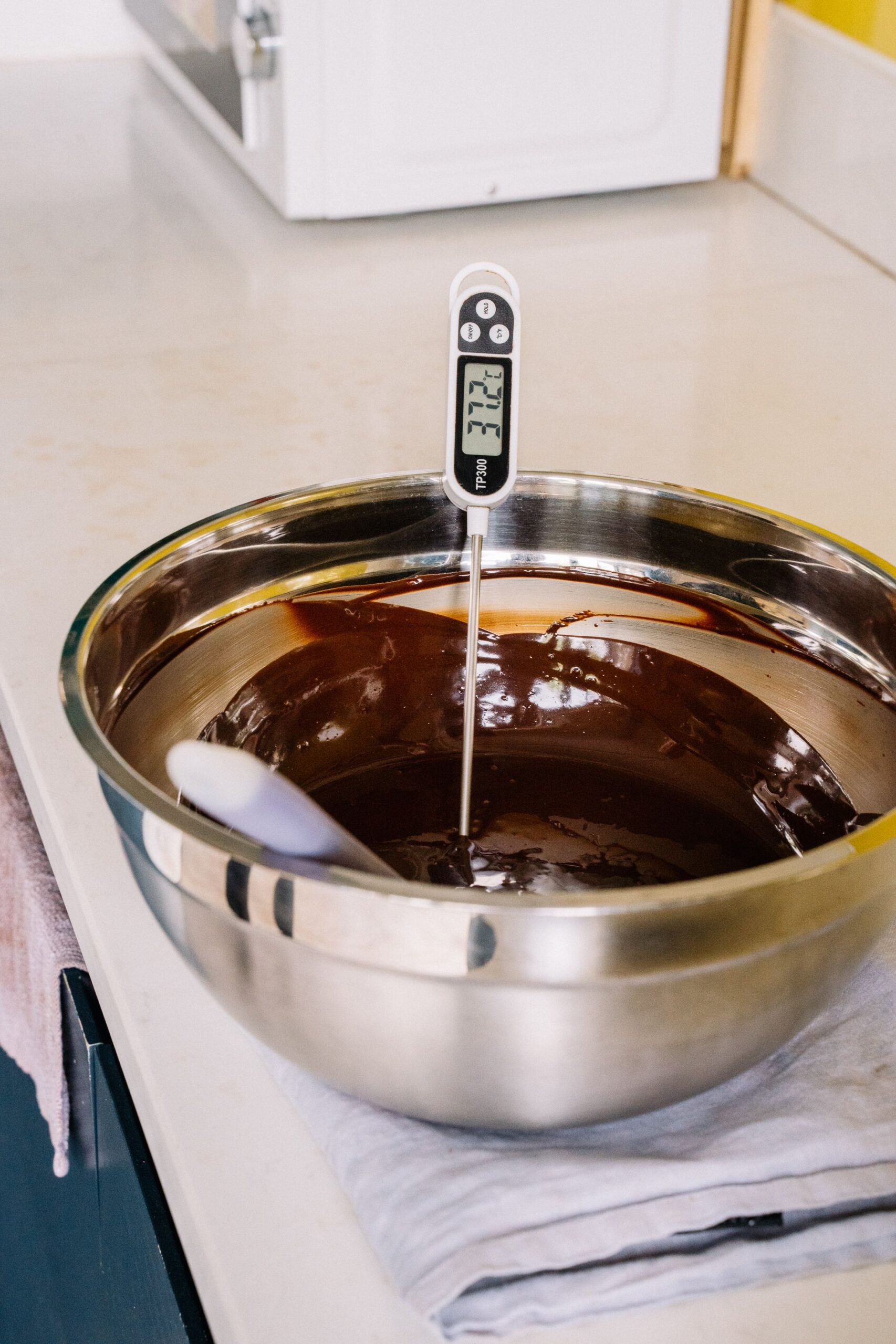 Digital thermometer resting in a bowl of melted chocolate