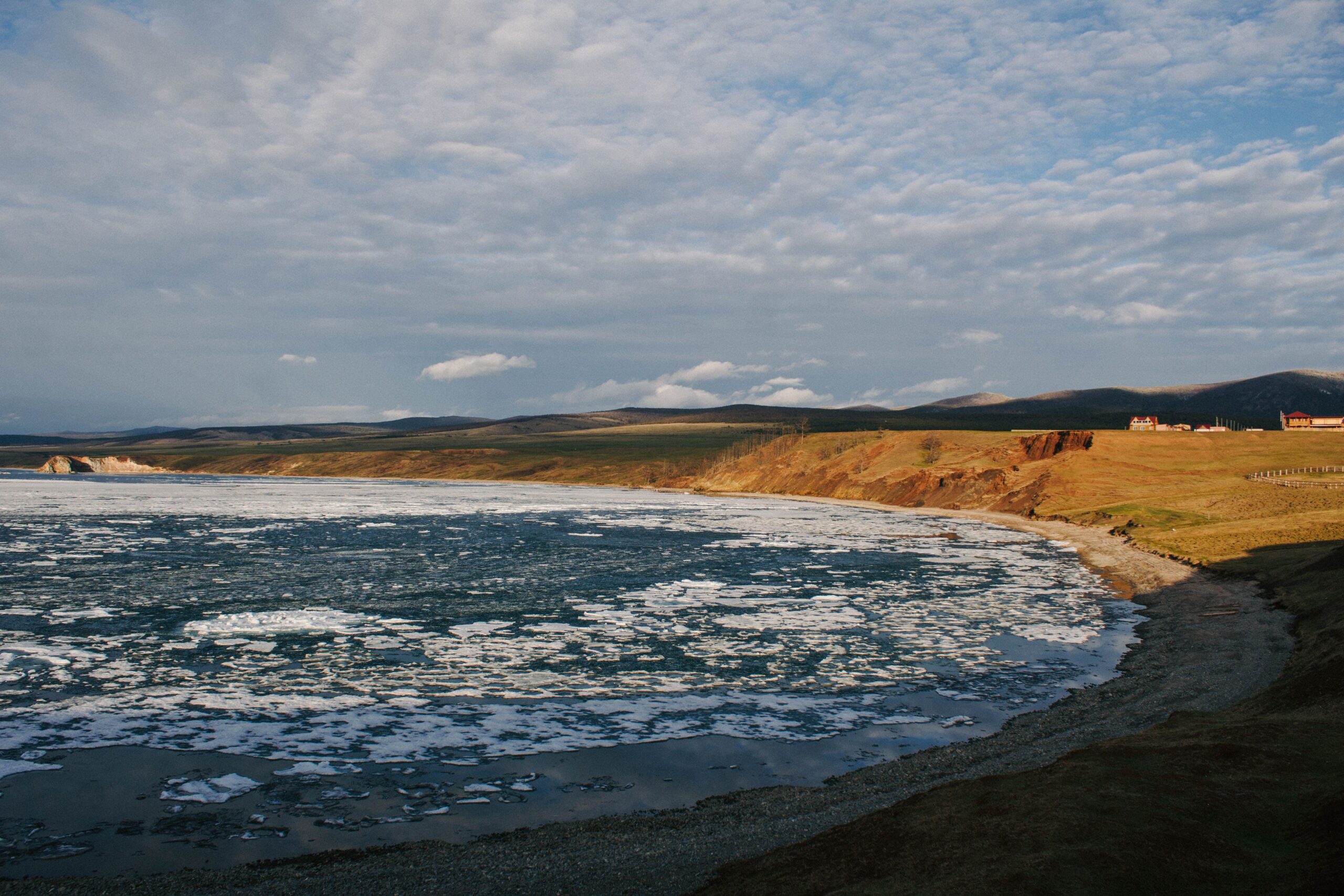 Sea ice floating near a remote coastline under a cloudy sky