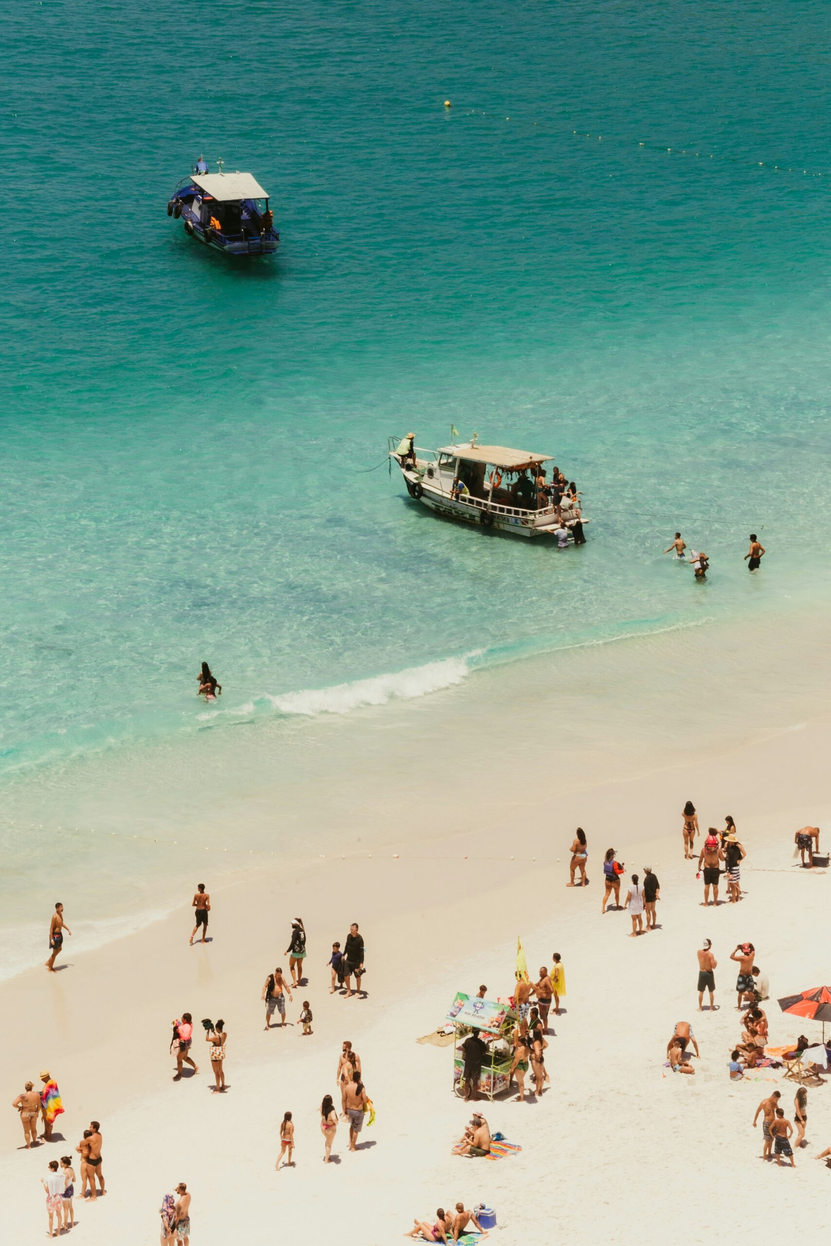 People swimming and relaxing at a busy tropical beach beside clear blue water