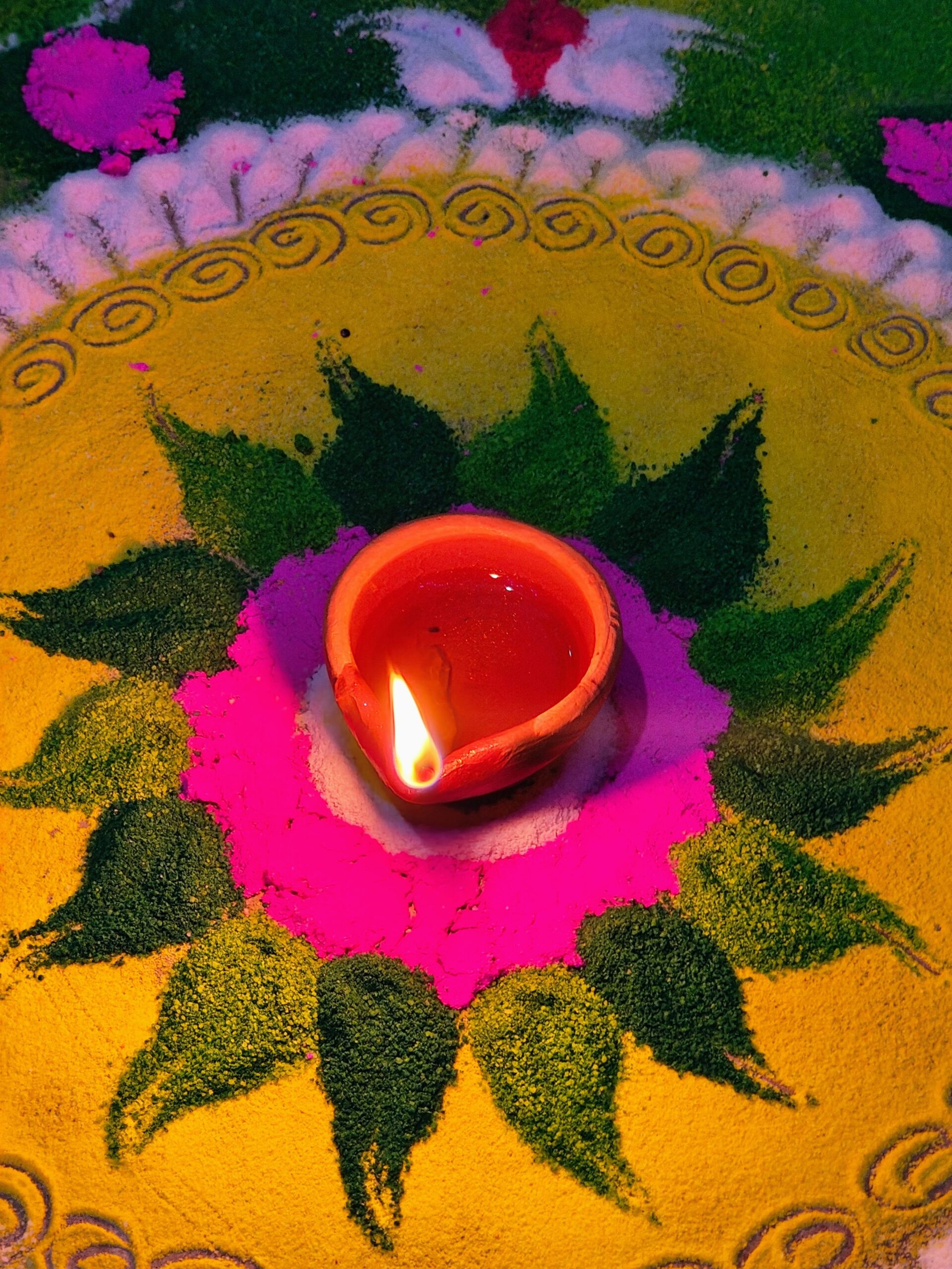 A colorful Diwali rangoli with a lit clay diya at its center