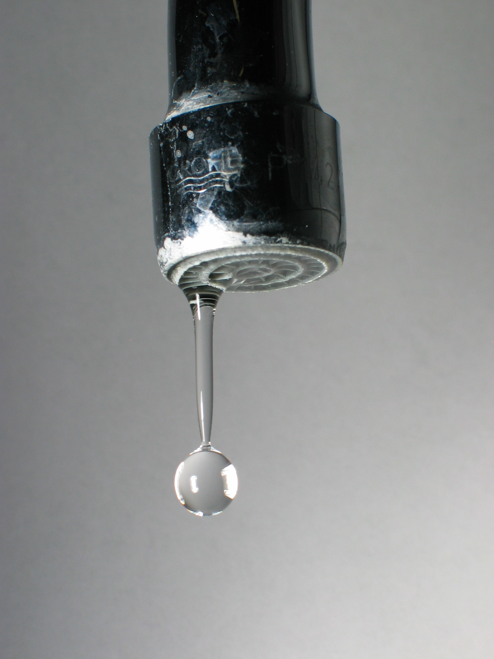 Single drop of water falling from a metal faucet