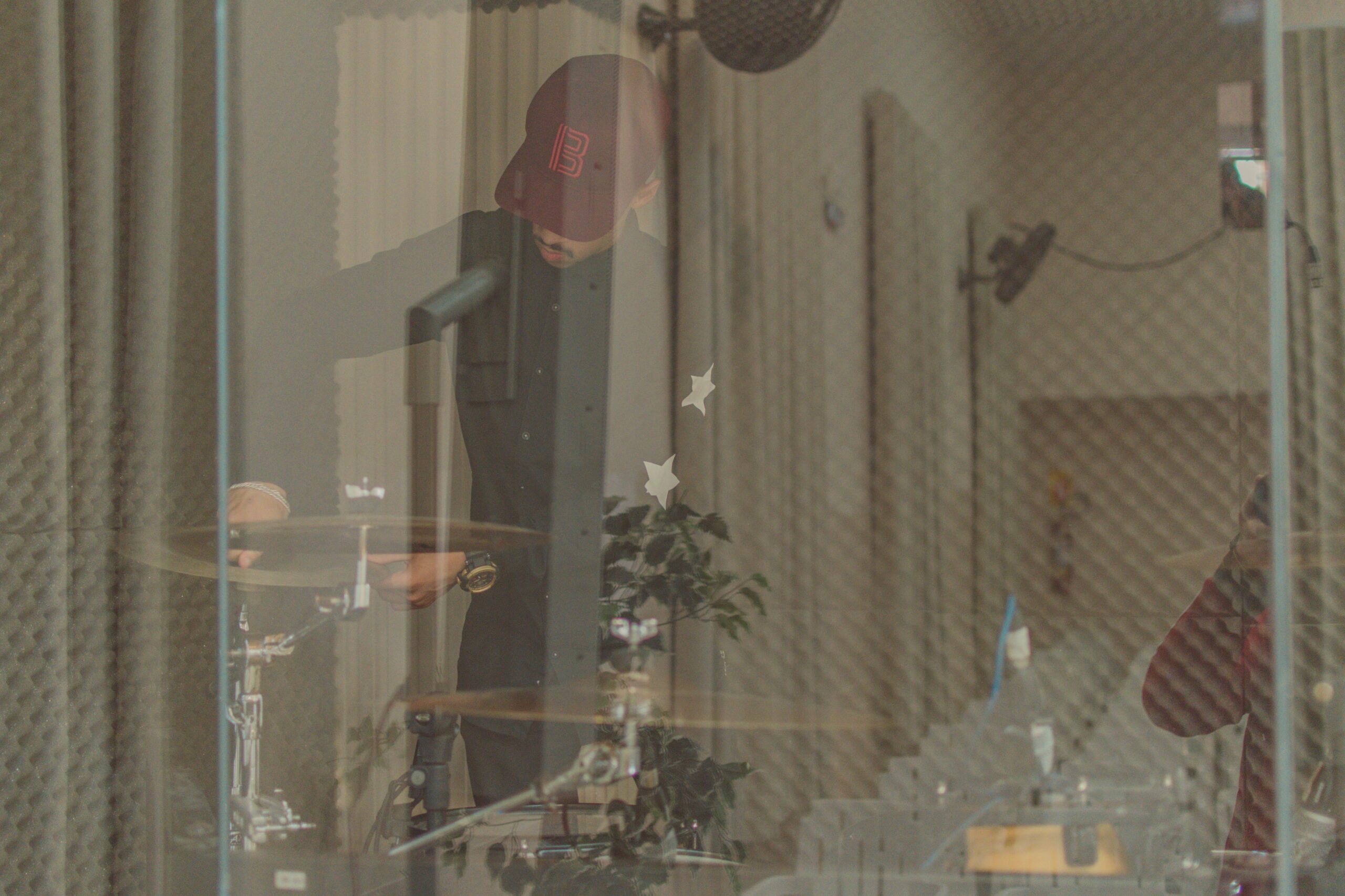 Drummer performing behind glass in an acoustically treated recording studio