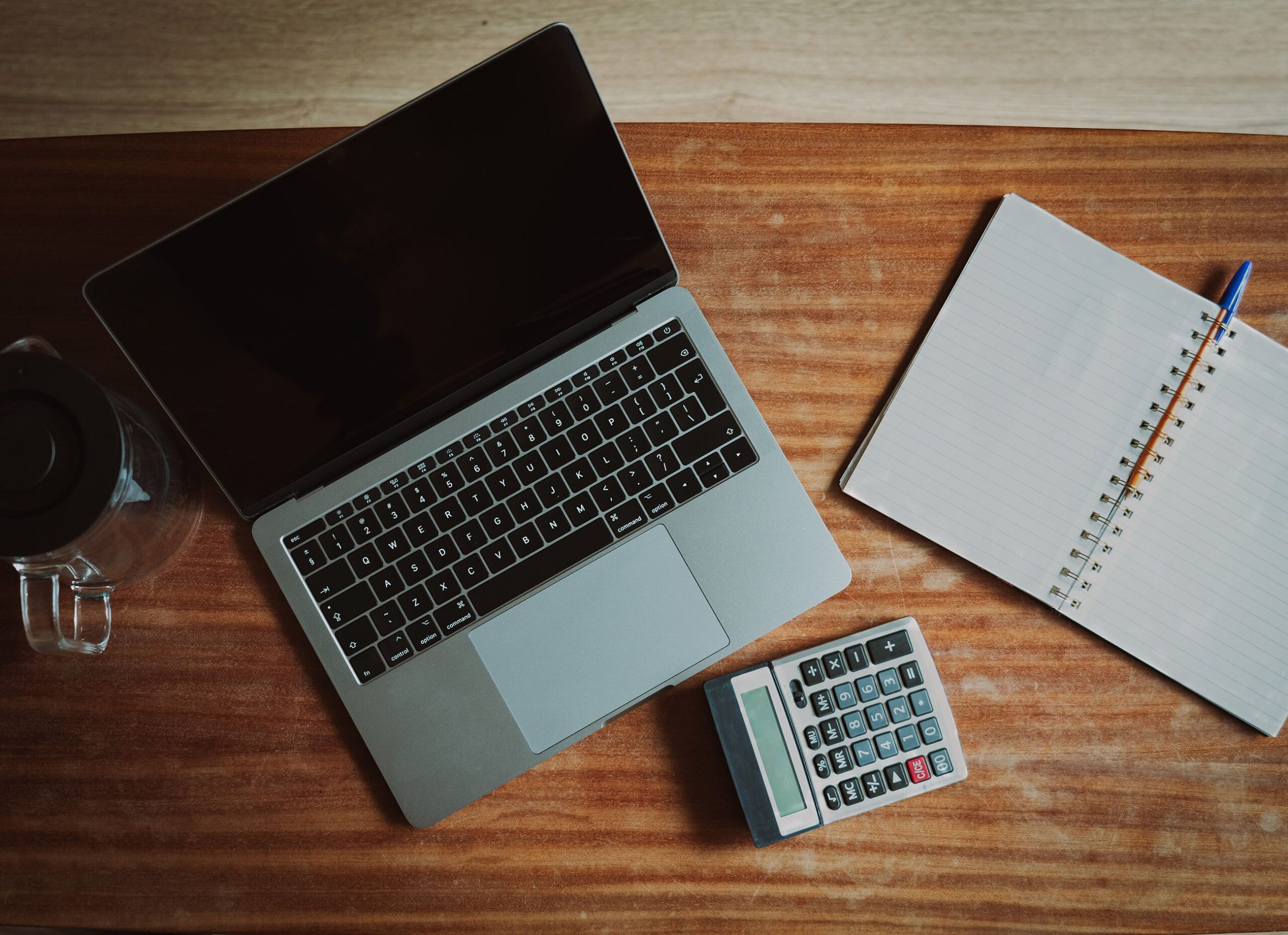 Laptop, calculator, notebook, and paperwork arranged on a desk