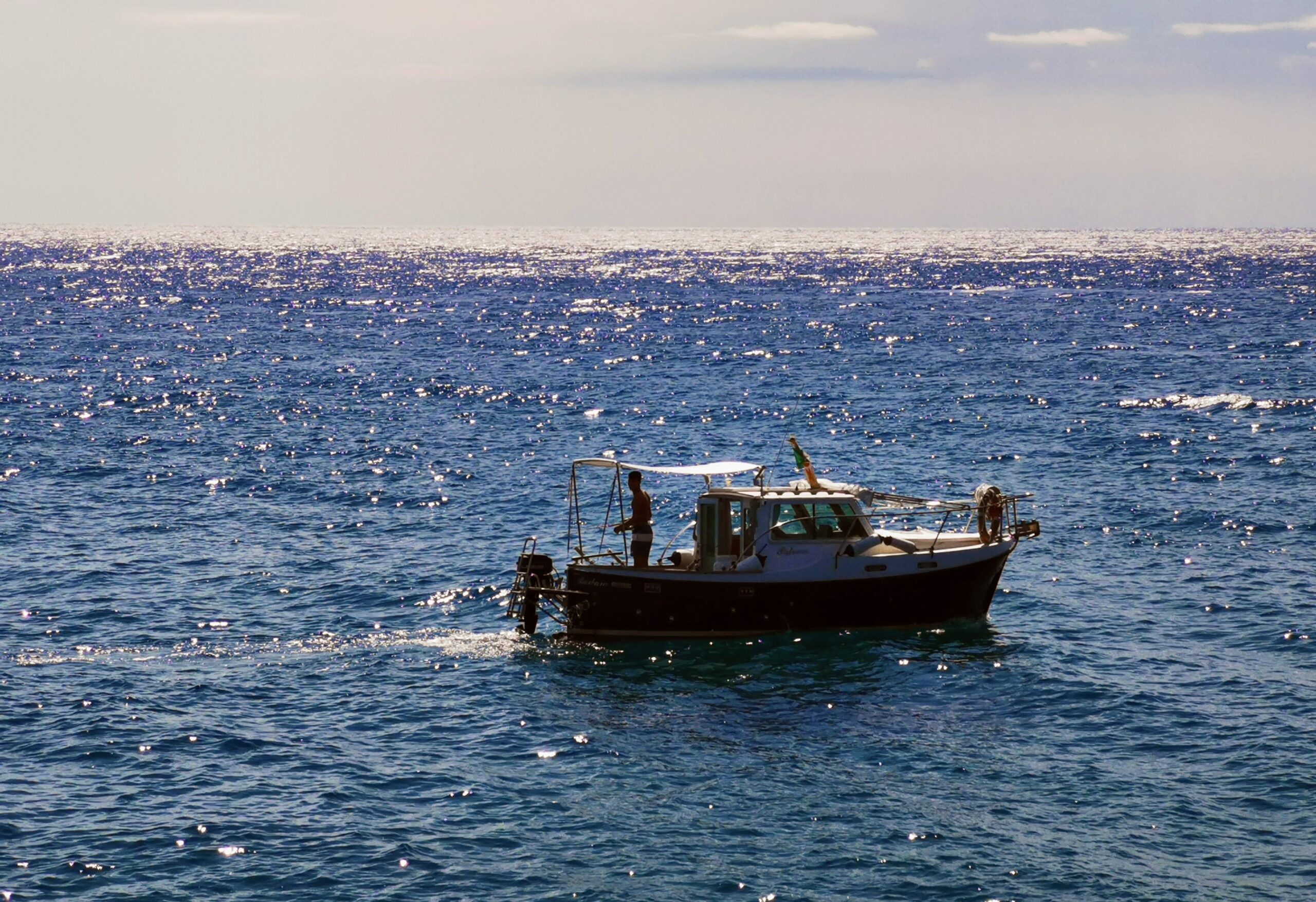 A fishing boat traveling across open ocean under a clear sky